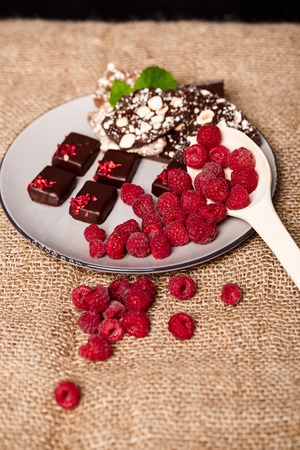 Chocolate candies and raspberry on white plate over sackcloth. Copy space.の写真素材