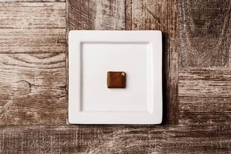 Chocolate candy on white plate over wooden background. From above. Copy space.