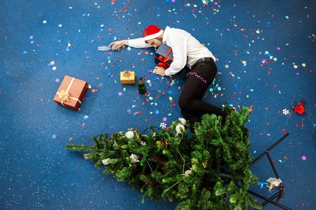 Young handsome businessman in red santa claus hat celebrating christmas in office sleeping on floor. Copy space.の写真素材