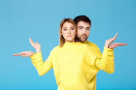 Young beautiful couple in one yellow sweater posing smiling having fun over blue background. Copy...