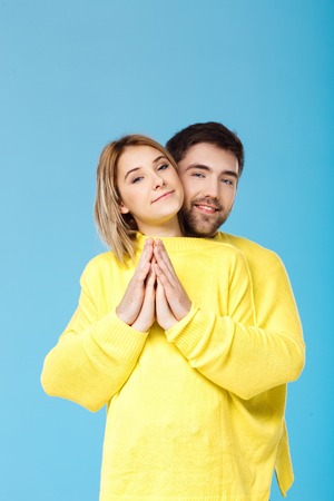 Young beautiful couple in one yellow sweater embracing smiling over blue background. Copy space.