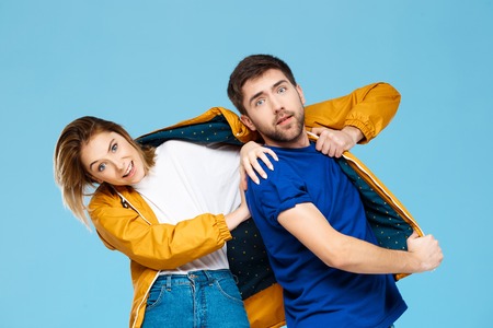 funny young beautiful couple wearing one jacket  over blue background. Copy space.の写真素材