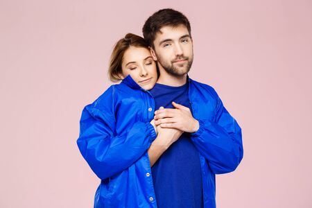 Funny young beautiful couple wearing one jacket embracing smiling over light pink background. Copy space.の写真素材