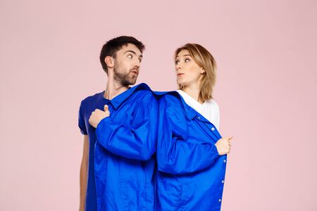 Funny young beautiful couple wearing one jacket  over light pink background. Copy spaceの写真素材
