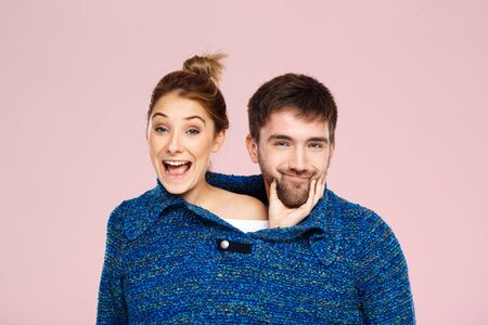 Young beautiful couple in one blue knitted sweater posing smiling having fun over light pink background. Copy space.の写真素材