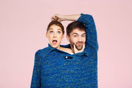 Young beautiful couple in one blue knitted sweater posing smiling having fun over light pink background. Copy space.の写真素材