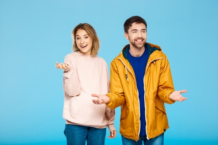 Young beautiful couple posing smiling having fun over blue background. Man wearing rain coat. Copy space.の写真素材
