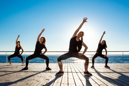 Silhouettes of sportive girls dancing zumba near sea at sunrise.の写真素材
