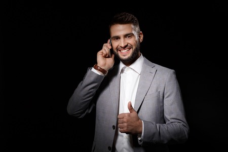 Young successful businessman smiling speaking on phone over black background.の写真素材