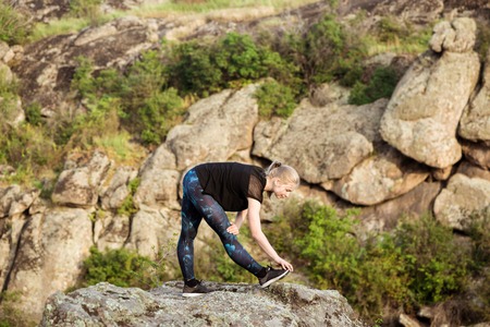 Beautiful sportive blonde girl training, stretching on rock in canyon.