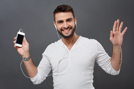 Young handsome man smiling holding phone over grey background.の写真素材