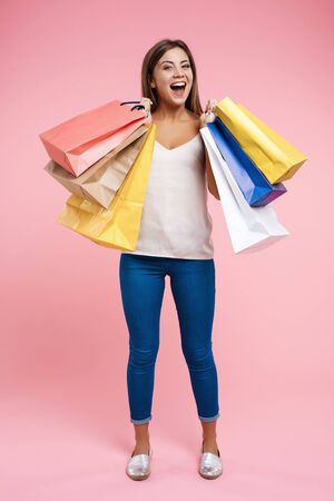 Happy young woman holding shopping bags staying on pink backgroundの写真素材