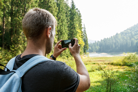 Young handsome man traveling, taking photo of beautiful mountains view.の写真素材