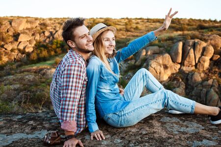 Young couple smiling, sitting on rock in canyon, enjoying view.の写真素材