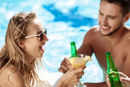 Friends speaking, smiling, drinking cocktails, resting, relaxing near swimming pool.