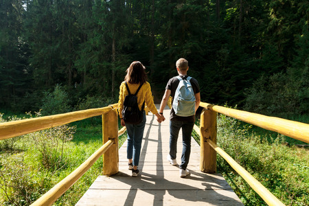 Young couple of travelers going on wooden bridge in mountains.の写真素材