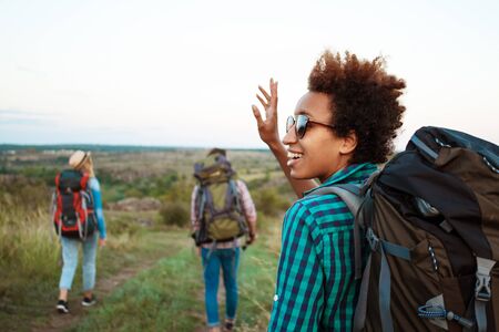 Beautiful african girl with backpack smiling, greeting, friends travelers background.の写真素材