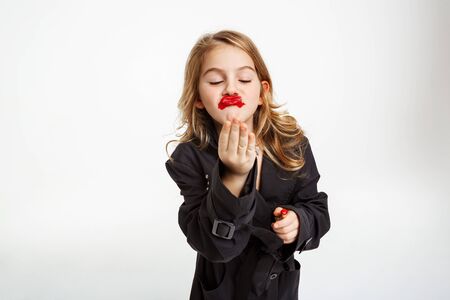 Funny girl with messy make up. Wearing fashion black trench air kissing, hoding red lipstick.の写真素材