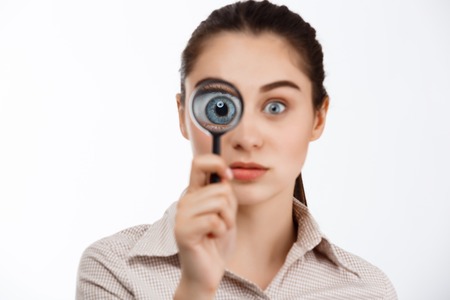 Young beautiful brunette girl looking at camera through magnifier over white background.の写真素材
