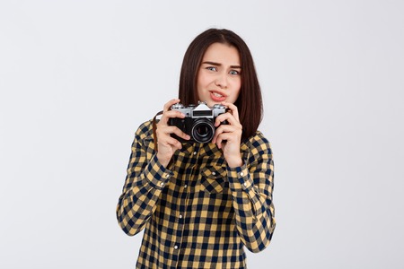 Young beautiful brunette photographer taking pictures, looking at camera over white background.の写真素材