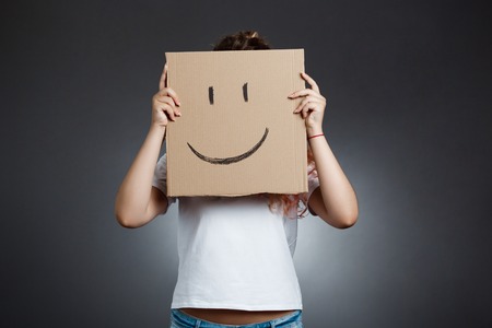 Young beautiful girl hiding head behind carton with smiley over grey background. Copy space.の写真素材