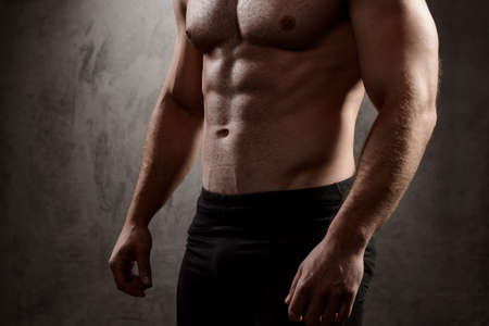 Close up photo of sportive man's body over dark background.