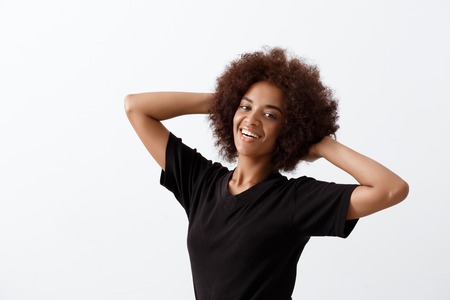 Young beautiful african girl smiling with hands behind head, looking at camera over light background. Copy space.の写真素材