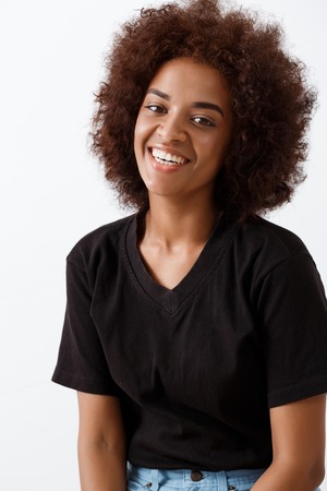 Young beautiful african girl smiling, looking at camera over light background.の写真素材