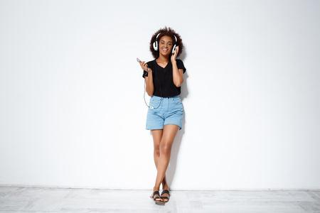 Young beautiful african girl listening music in headphones, singing over white background. Copy space.の写真素材