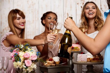 Four young beautiful girls in dresses holding glasses with champagne, speaking, smiling, laughing, resting at party.の写真素材