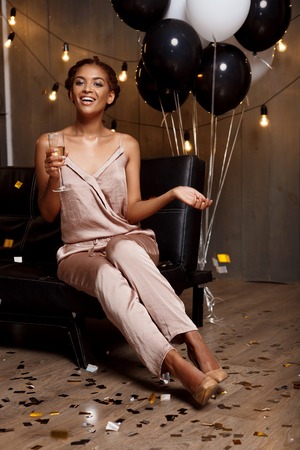 Portrait of young beautiful african girl looking at camera, smiling, laughing, holding glass with champagne, resting at party.の写真素材