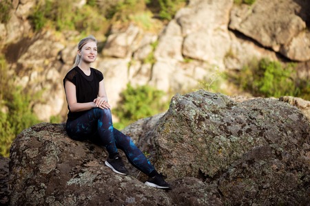 Young beautiful sportive girl smiling, sitting on rock in canyon.の写真素材