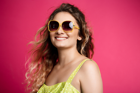 Young beautiful girl in sunglasses smiling over pink background.の写真素材