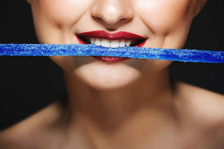 Closeup picture of cheerful girls lips holding sweeties with teeth.の写真素材