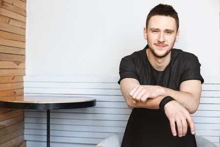 Young man sitting on chair with hands on chair back.の写真素材