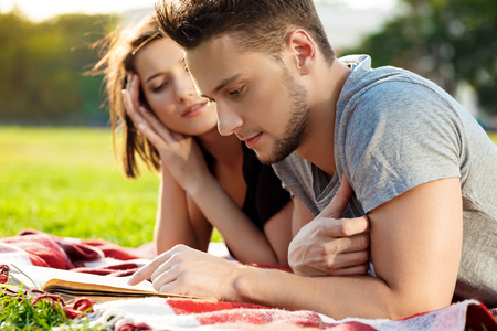 Young beautiful couple smiling, reading, resting on picnic in park.の写真素材