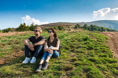 Young couple smiling, enjoying mountains lanscape, sitting on hill.の写真素材