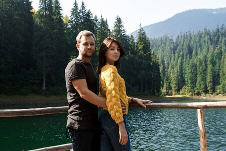 Young beautiful couple smiling, embracing, lake and mountains background.の写真素材