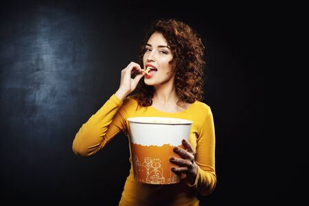 Attractive woman eating cheesy popcorn looking pleased and happyの写真素材