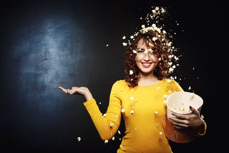Attractive young woman staying under popcorn shower with hand upの写真素材