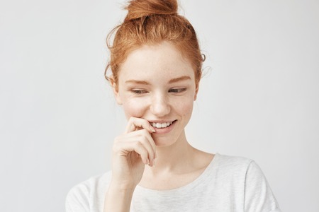 Portrait of shy beautiful girl with foxy hair and freckles smiling.