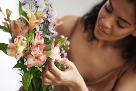 Beautiful african female florist making bouquet of flowers preparing to sell them. Focus on alstroemerias. Young entrepreneur.の写真素材