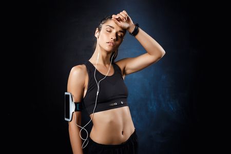 Young beautiful sportive girl listening music over dark background.の写真素材