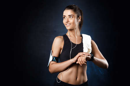 Young beautiful sportive girl listening music over dark background.