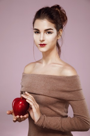Beautiful girl smiling looking at camera holding red apple over pink background.の写真素材