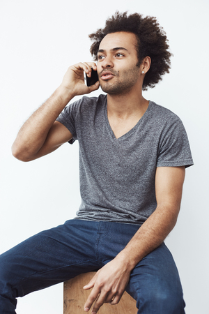 Young african man talking on phone sitting over white background.の写真素材