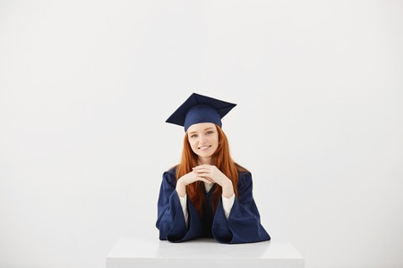 Beautiful ginger graduate smiling looking at camera sitting over white background.の写真素材