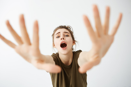 Emotive young girl looking stretching hands to camera with opened mouth over white background.の写真素材