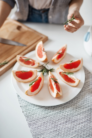 Close up of girl decorating plate with sliced grapefruit and rosemary. Healthy nutrition concept. Copy space.の写真素材