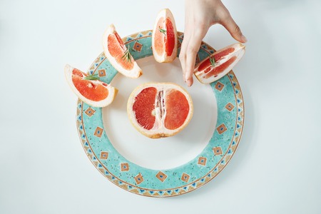 Girls hand taking slice of grapefruit from white plate. From above. Healthy diet nutrition.の写真素材